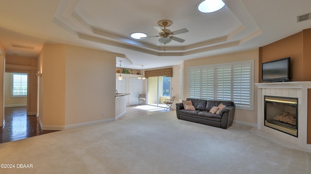 carpeted living room with a tiled fireplace, ceiling fan, and a tray ceiling