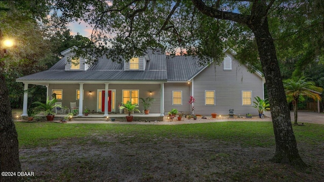 back house at dusk featuring a porch and a yard