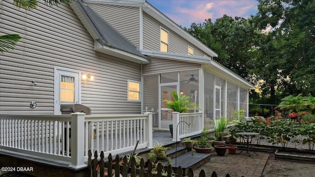 back house at dusk featuring a sunroom, a wooden deck, and a patio area