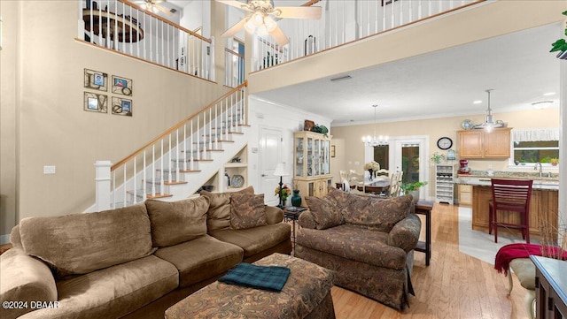 living room featuring a high ceiling, ceiling fan with notable chandelier, ornamental molding, and light hardwood / wood-style flooring