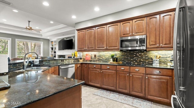 kitchen featuring sink, dark stone countertops, stainless steel appliances, a tray ceiling, and kitchen peninsula