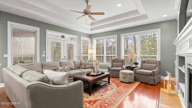 living room featuring french doors, ceiling fan, a tray ceiling, crown molding, and light hardwood / wood-style flooring