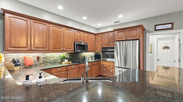 kitchen with stainless steel appliances, sink, dark stone countertops, and backsplash