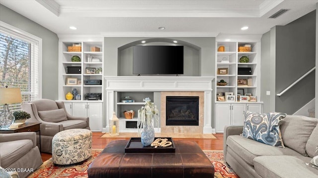 living room featuring wood-type flooring, built in shelves, crown molding, and a tray ceiling