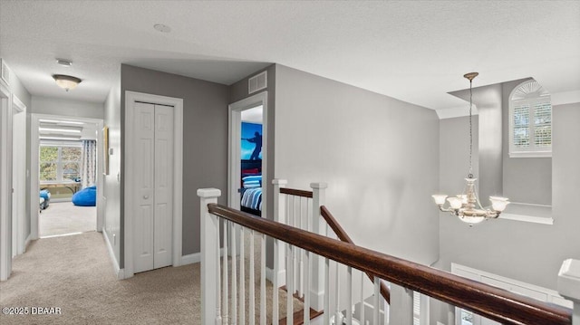 corridor featuring light colored carpet, a textured ceiling, and an inviting chandelier