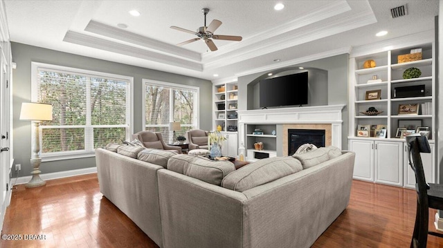 living room featuring dark hardwood / wood-style flooring, ornamental molding, built in features, and a raised ceiling