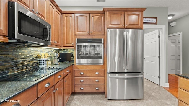 kitchen featuring backsplash, appliances with stainless steel finishes, light tile patterned floors, and dark stone countertops