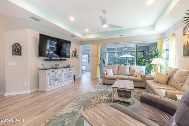 living room featuring ceiling fan, a raised ceiling, and light wood-type flooring