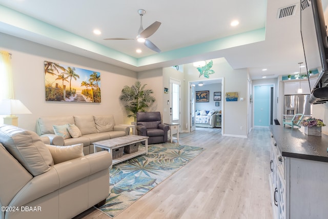 living room featuring light hardwood / wood-style floors, ceiling fan, and a raised ceiling