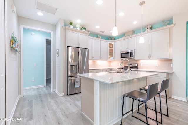 kitchen with stainless steel appliances, light hardwood / wood-style floors, white cabinets, hanging light fixtures, and an island with sink