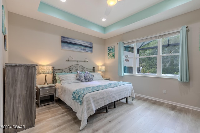 bedroom featuring light hardwood / wood-style flooring, ceiling fan, and a tray ceiling