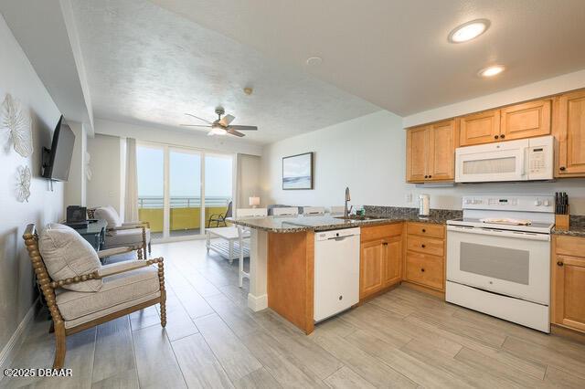 kitchen with a peninsula, white appliances, light wood-style flooring, and a sink