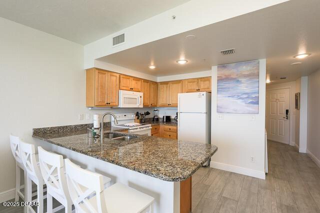 kitchen featuring dark stone counters, a sink, light wood-type flooring, white appliances, and a peninsula