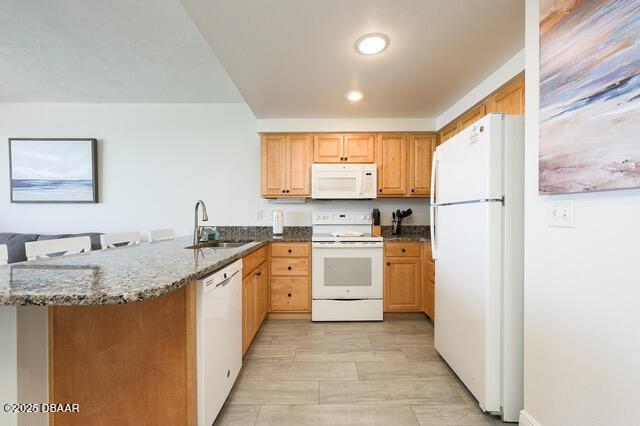 kitchen with recessed lighting, a sink, dark stone counters, white appliances, and a peninsula