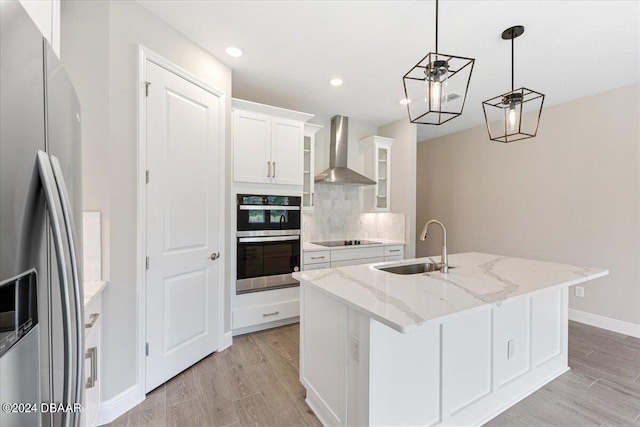 kitchen with wall chimney range hood, white cabinets, a kitchen island with sink, and stainless steel appliances