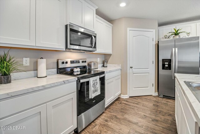 kitchen with light stone counters, light hardwood / wood-style flooring, white cabinets, and appliances with stainless steel finishes