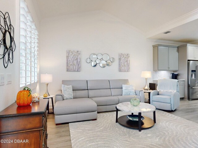 living room featuring ornamental molding, lofted ceiling, light wood-type flooring, and visible vents