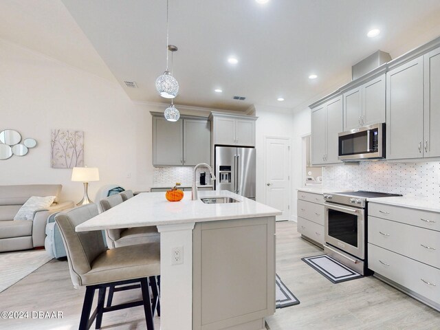 kitchen with a kitchen bar, gray cabinetry, a sink, light wood-style floors, and premium appliances