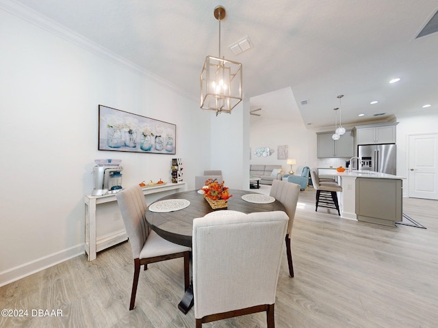 dining area featuring visible vents, light wood finished floors, crown molding, and a notable chandelier