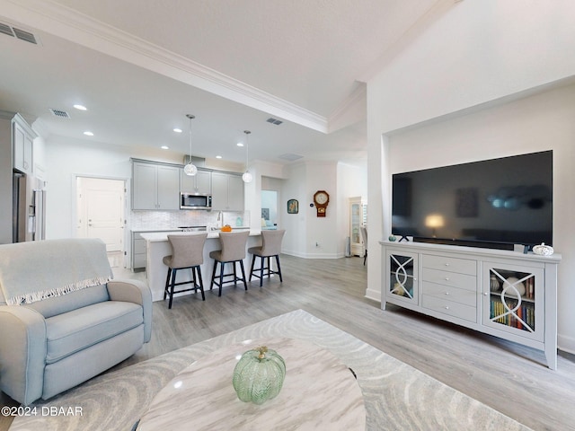 living room featuring crown molding, visible vents, baseboards, recessed lighting, and light wood finished floors