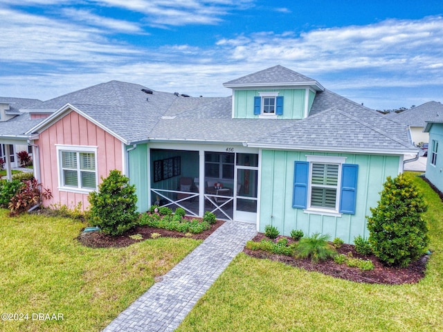 view of front of property featuring roof with shingles, board and batten siding, a sunroom, and a front lawn