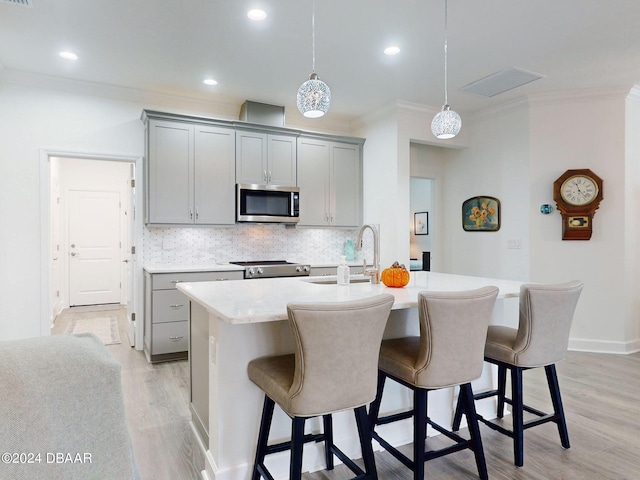 kitchen featuring gray cabinets, a breakfast bar area, appliances with stainless steel finishes, a sink, and ornamental molding