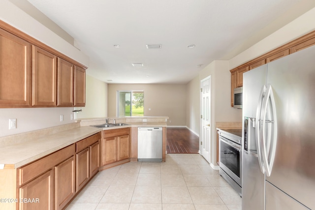 kitchen featuring kitchen peninsula, appliances with stainless steel finishes, sink, and light tile patterned floors