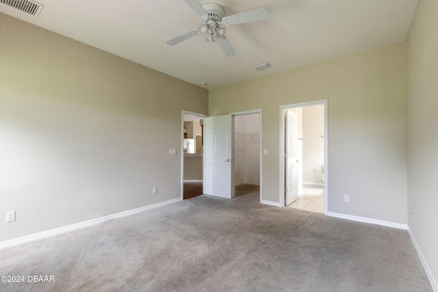 unfurnished bedroom featuring ensuite bath, ceiling fan, a walk in closet, light colored carpet, and a closet