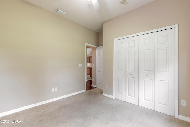 unfurnished bedroom with ceiling fan, light carpet, a closet, and a textured ceiling