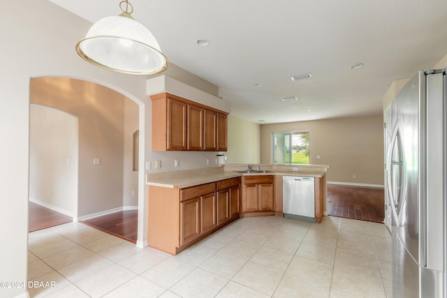 kitchen with appliances with stainless steel finishes, pendant lighting, sink, kitchen peninsula, and light hardwood / wood-style flooring