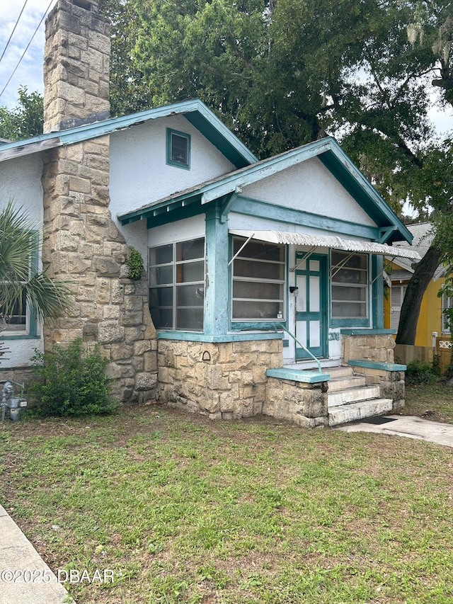 208 Bellevue Ave, Daytona Beach, FL 32114 - view of front facade with stucco siding, stone siding, a front lawn, and a chimney