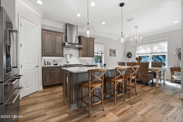 kitchen with a center island with sink, a breakfast bar, ornamental molding, wall chimney exhaust hood, and stainless steel fridge