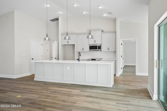 kitchen with light hardwood / wood-style floors, white cabinetry, a center island with sink, decorative light fixtures, and high vaulted ceiling