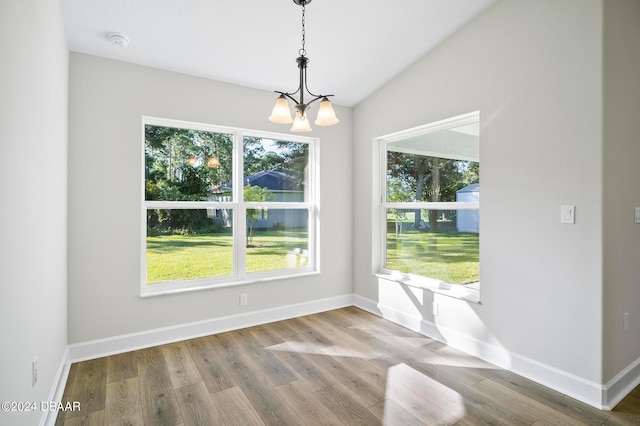 unfurnished dining area with hardwood / wood-style floors, a wealth of natural light, lofted ceiling, and an inviting chandelier