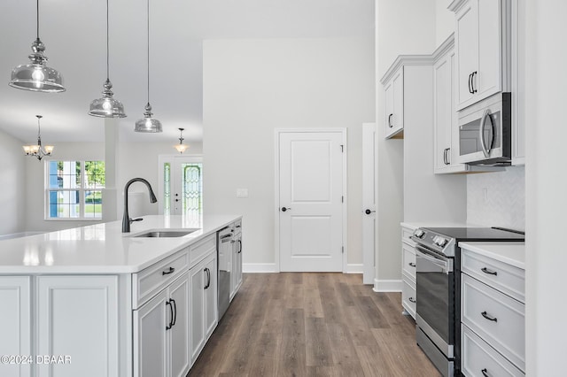 kitchen with stainless steel appliances, white cabinetry, hanging light fixtures, sink, and an island with sink