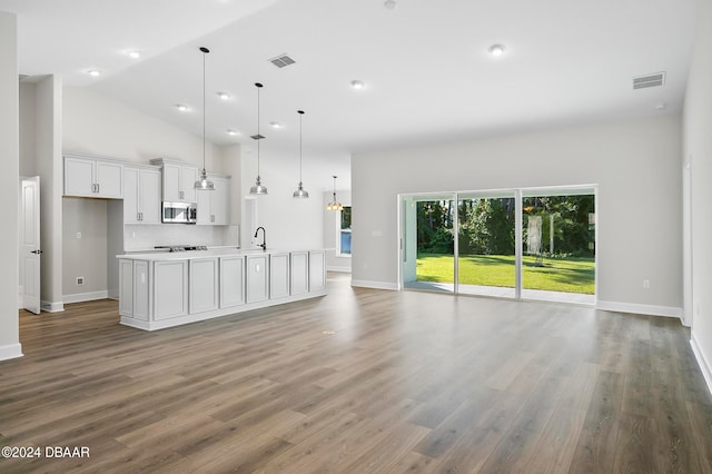 kitchen with stainless steel appliances, an island with sink, hanging light fixtures, wood-type flooring, and white cabinets