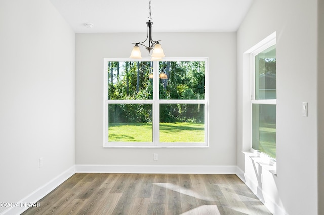 unfurnished dining area featuring wood-type flooring, a healthy amount of sunlight, and a notable chandelier