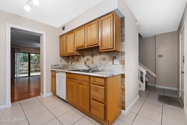 kitchen featuring dishwasher, sink, decorative backsplash, light tile patterned floors, and light stone counters