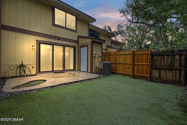 back house at dusk with a yard, a patio, and central AC unit