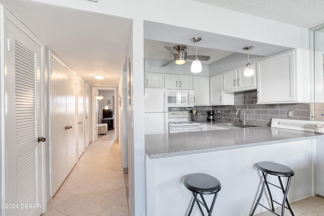 kitchen with sink, a kitchen breakfast bar, light tile patterned flooring, white cabinetry, and white appliances