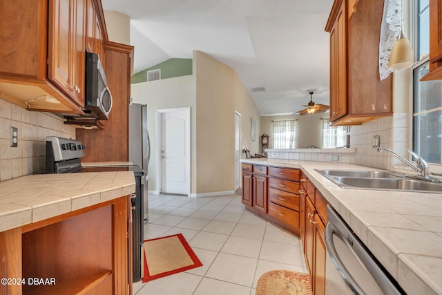 kitchen featuring appliances with stainless steel finishes, tasteful backsplash, vaulted ceiling, sink, and tile countertops