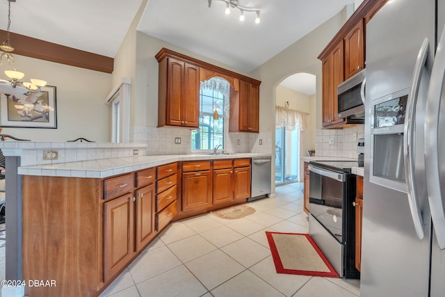 kitchen with appliances with stainless steel finishes, tasteful backsplash, light tile patterned floors, and hanging light fixtures