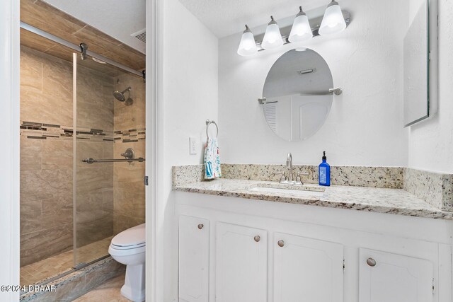 bathroom with toilet, vanity, a textured ceiling, and a tile shower