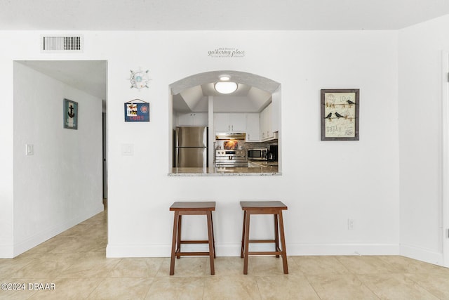 kitchen with light stone counters, white cabinets, kitchen peninsula, light tile patterned floors, and appliances with stainless steel finishes