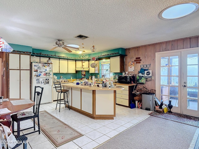 kitchen featuring visible vents, wood walls, freestanding refrigerator, a textured ceiling, and a ceiling fan