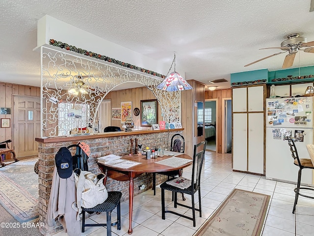 dining space featuring wooden walls, light tile patterned floors, a ceiling fan, and a textured ceiling