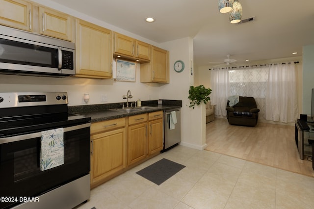 kitchen with appliances with stainless steel finishes, light brown cabinetry, ceiling fan, sink, and light hardwood / wood-style flooring