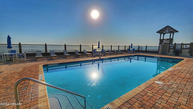 pool at dusk featuring a water view and a patio