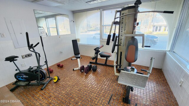 exercise room featuring dark tile patterned flooring and tile walls