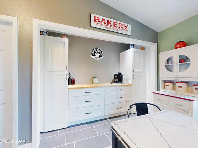 kitchen with light tile patterned flooring, white cabinetry, and vaulted ceiling